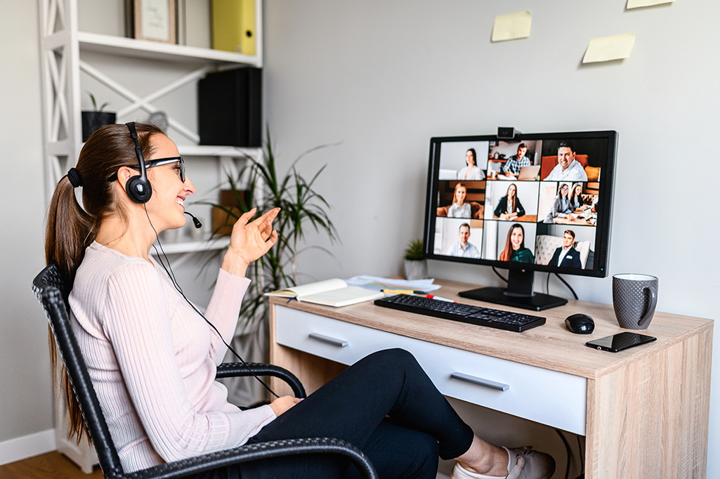 A photo of a happy woman on a video call with 9 other people in a home office.